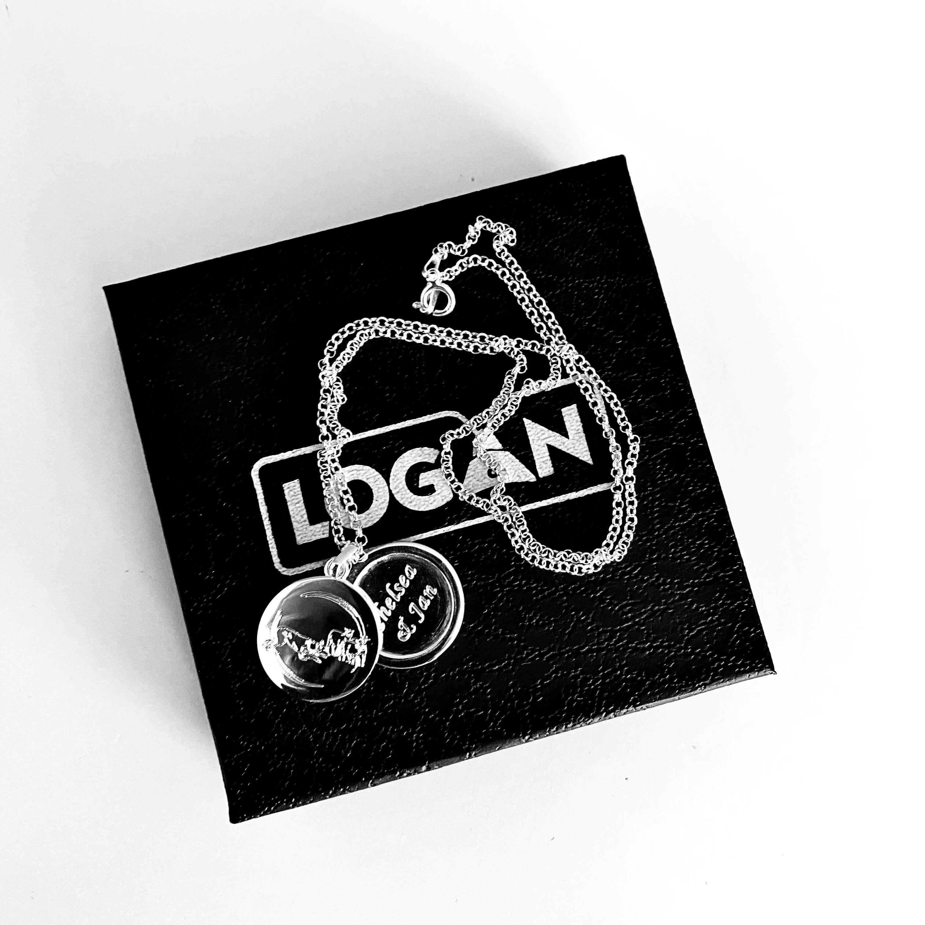 Silver necklace with two discs on a black box with 'LOGAN' branding.