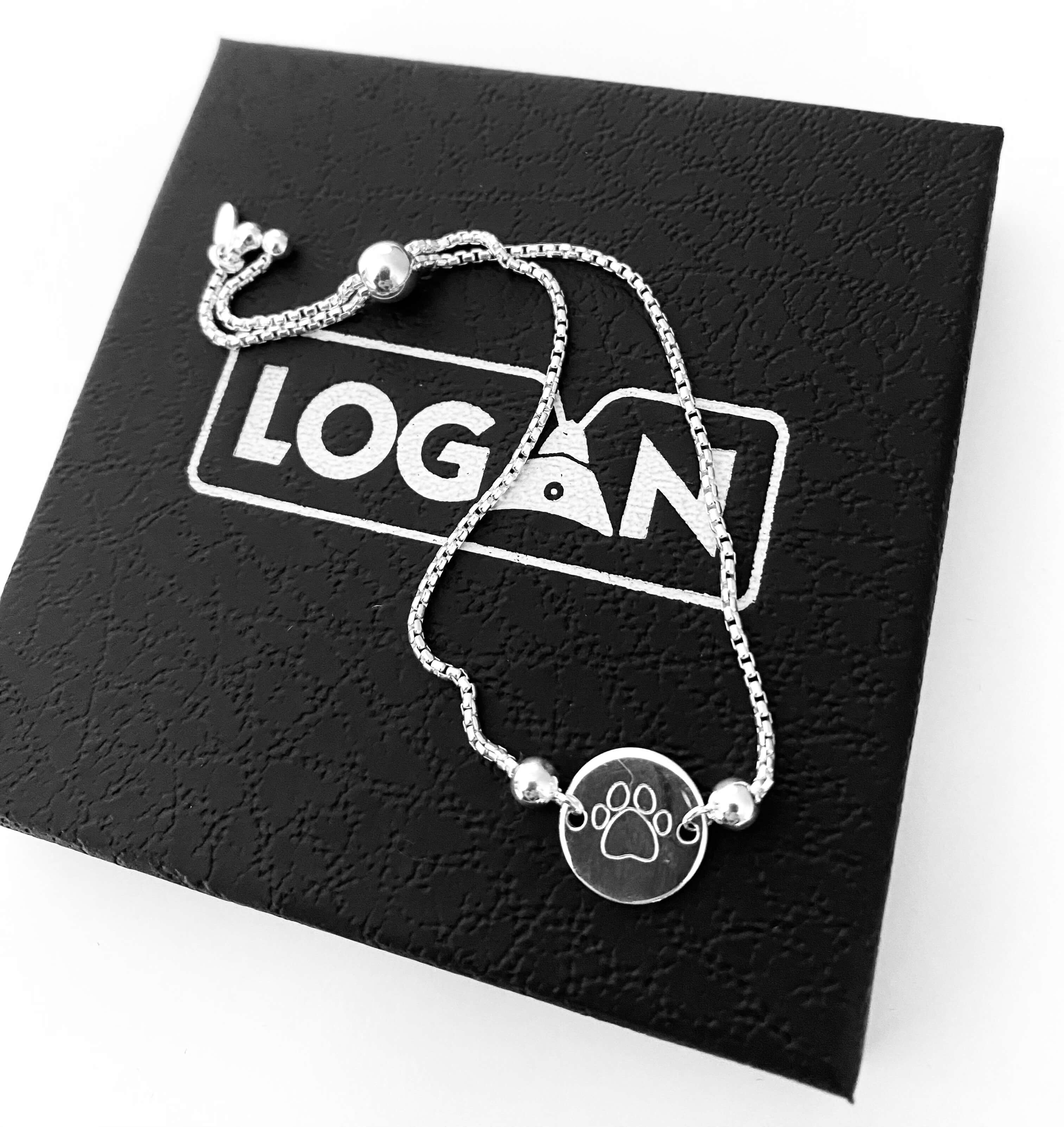 Silver bracelet with paw print charm on a black card with 'LOGAN' printed on it.