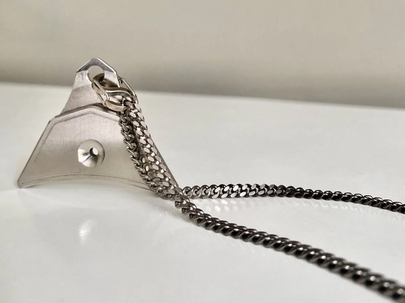 Silver sheepdog whistle pendant attached to a chain on a white surface.