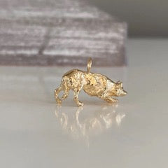 A small gold border collie charm standing on a glossy white surface with a blurred gray background.