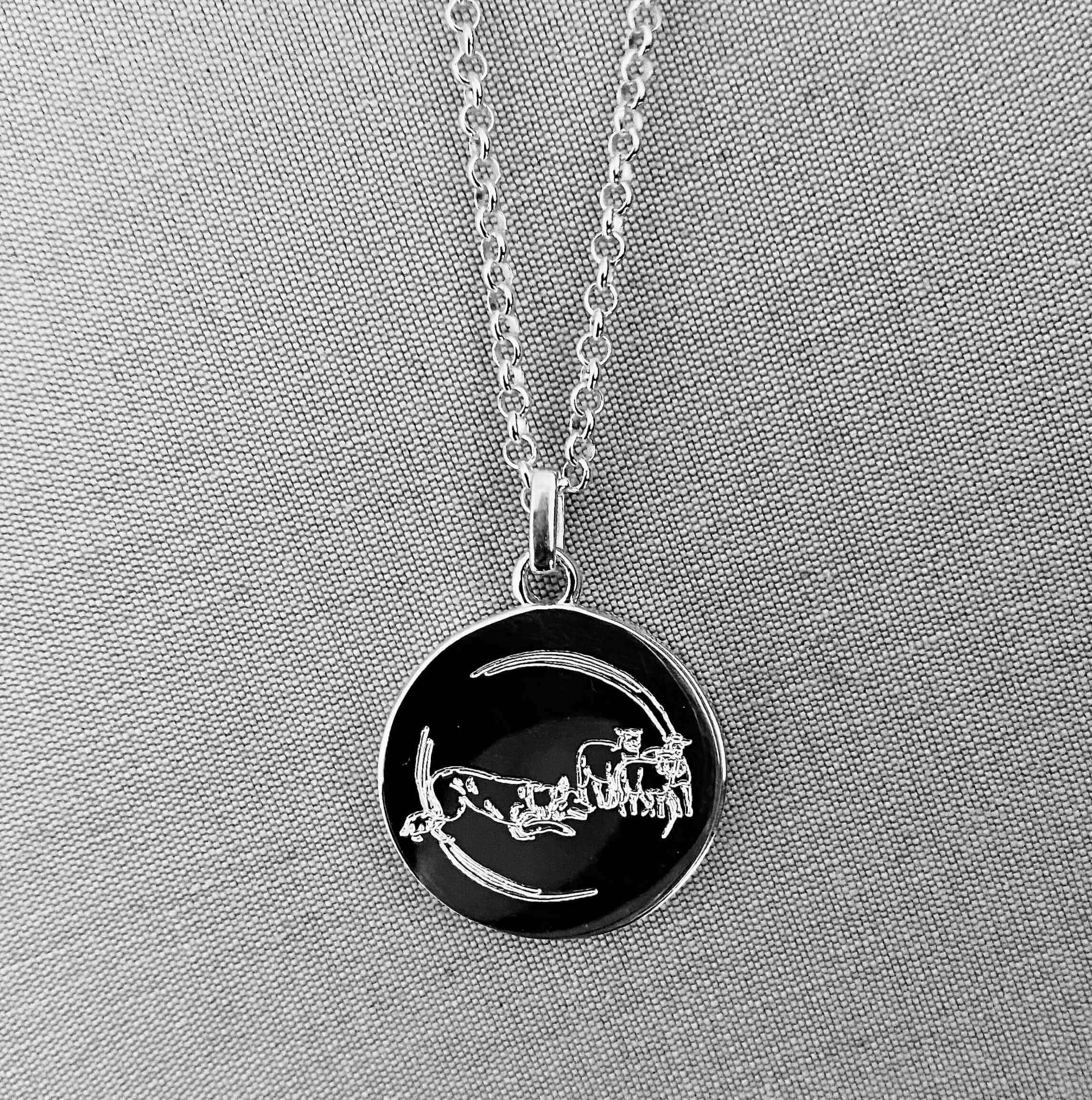 Silver pendant with dog and sheep illustration on a gray fabric background