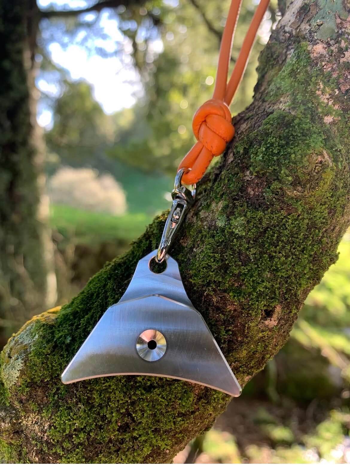 Logan 304 stainless steel whistle on orange leather lanyard against a tree branch